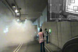  Example of a female candidate (on the right), who is attempting to transmit an emergency call via an escapeway sign. A test supervisor wearing a safety vest observes the participant. The simulated accident can be seen in the background. The section of the picture above right shows the situation as seen by the candidate 